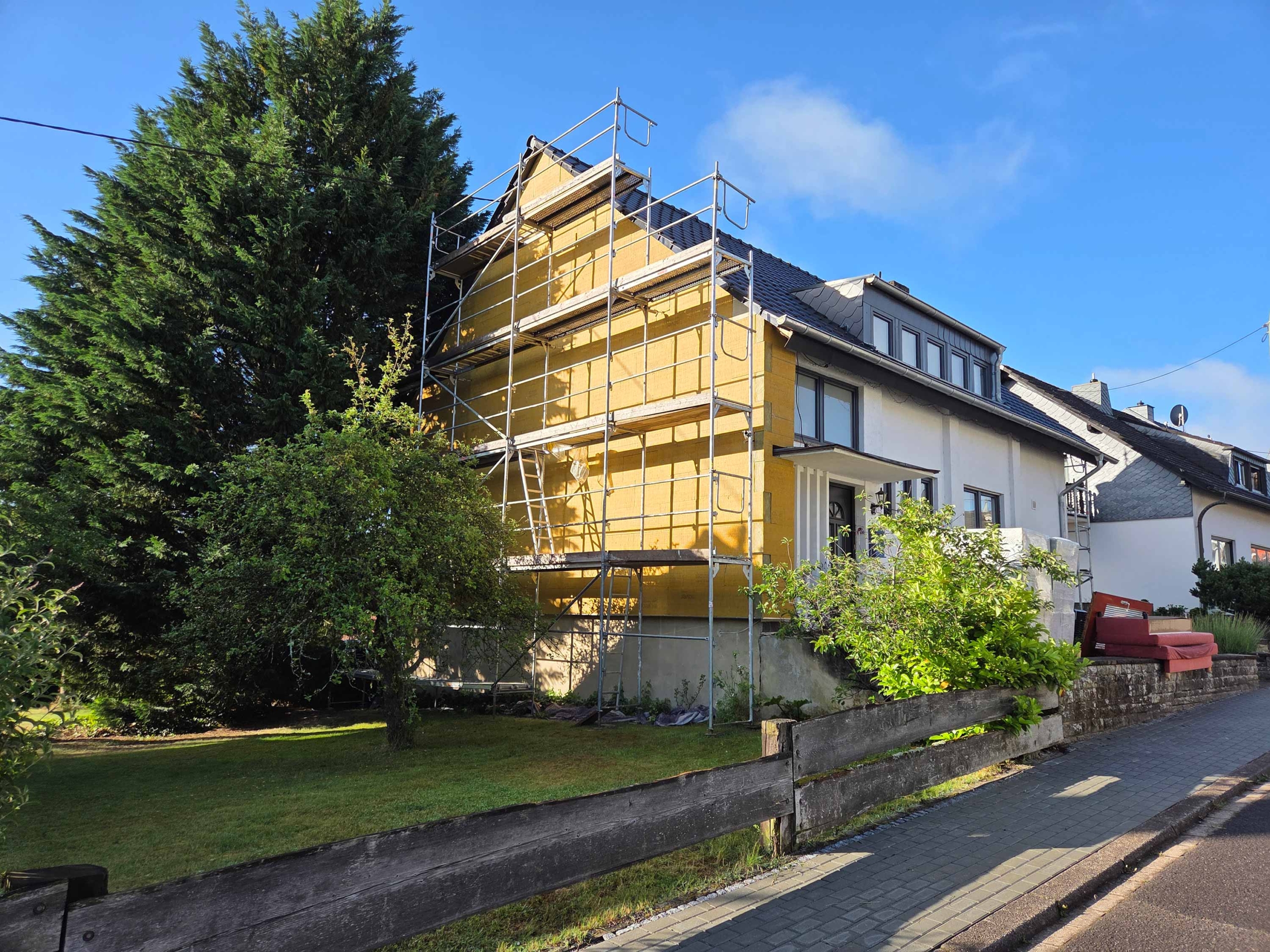Fassade eines Einfamilienhauses, bei dem die linke Hausseite mit gelber Mineralwolle gedämmt wurde. Am Haus steht noch ein Gerüst.